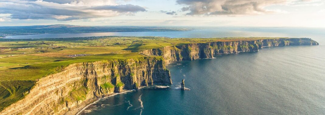 En el condado de Kerry, el Atlántico te invita a perderte en sus aguas infinitas. Desde un barco, te adentras once kilómetros mar adentro hasta contemplar los restos del antiguo enclave monástico de Skellig Michael, erguido sobre la roca como un guardián de siglos pasados, cuyo silencio y aislamiento le han valido el reconocimiento de Patrimonio de la Humanidad por la UNESCO. Cada ola que rompe contra los acantilados parece susurrar las historias de los monjes que vivieron allí, mientras el viento salado acaricia tu rostro y el aroma del mar llena tus pulmones. Un pedazo de historia más cercana aguarda en las islas Blasket, frente a Slea Head. Entre casas deshabitadas desde 1954, los senderos de la isla conservan el eco de vidas pasadas, donde cada piedra, cada puerta cerrada y cada ventana vacía parece narrar historias de familias que una vez llamaron a la isla su hogar. Caminar allí es como atravesar un umbral entre el tiempo presente y un pasado tangible, con el viento del Atlántico aleteando entre tus pasos. Si prefieres la grandiosidad del océano en estado puro, el faro de Fastnet, frente a la costa de Cork, se alza sobre una roca solitaria, batida por olas que rugen con fuerza y arremeten contra su base. Es el faro más indómito de Irlanda, un símbolo de resistencia frente a la inmensidad del mar y la furia de la naturaleza. Y para cerrar el viaje con un toque de magia, dirígete a Irlanda del Norte y contempla el castillo de Dunluce, encaramado al borde de los acantilados de Antrim. Sus muros antiguos y sus torres desafiantes parecen sacados de un cuento de hadas, donde la historia, el viento y el mar se entrelazan en un espectáculo que deja sin aliento. Cada rincón de este castillo costero respira leyenda, cada grieta en la piedra cuenta secretos de siglos, y el rugido constante del océano sirve como banda sonora de un lugar donde la naturaleza y la historia se funden en un abrazo épico.
